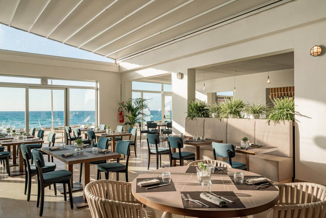 Sala ristorante al tramonto con vista mare, fotografata da un fotografo specializzato in hotel a Cagliari. Immagine che cattura l'atmosfera elegante e suggestiva della sala, con il panorama marino sullo sfondo.