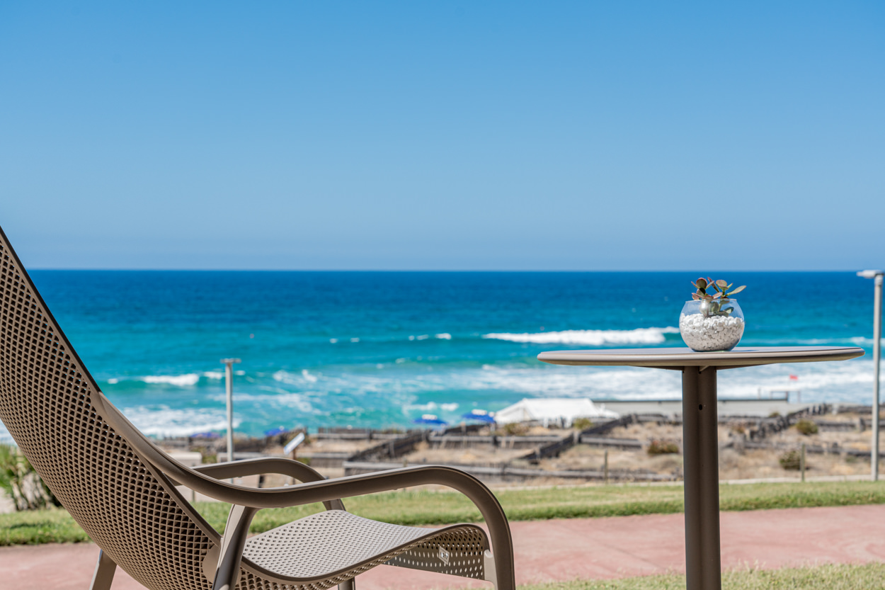 Scorcio di sedia e tavolino con vista mare, catturato da un fotografo specializzato in hotel e architettura in Sardegna. Foto che evidenzia il design elegante e l'atmosfera rilassante degli spazi esterni.