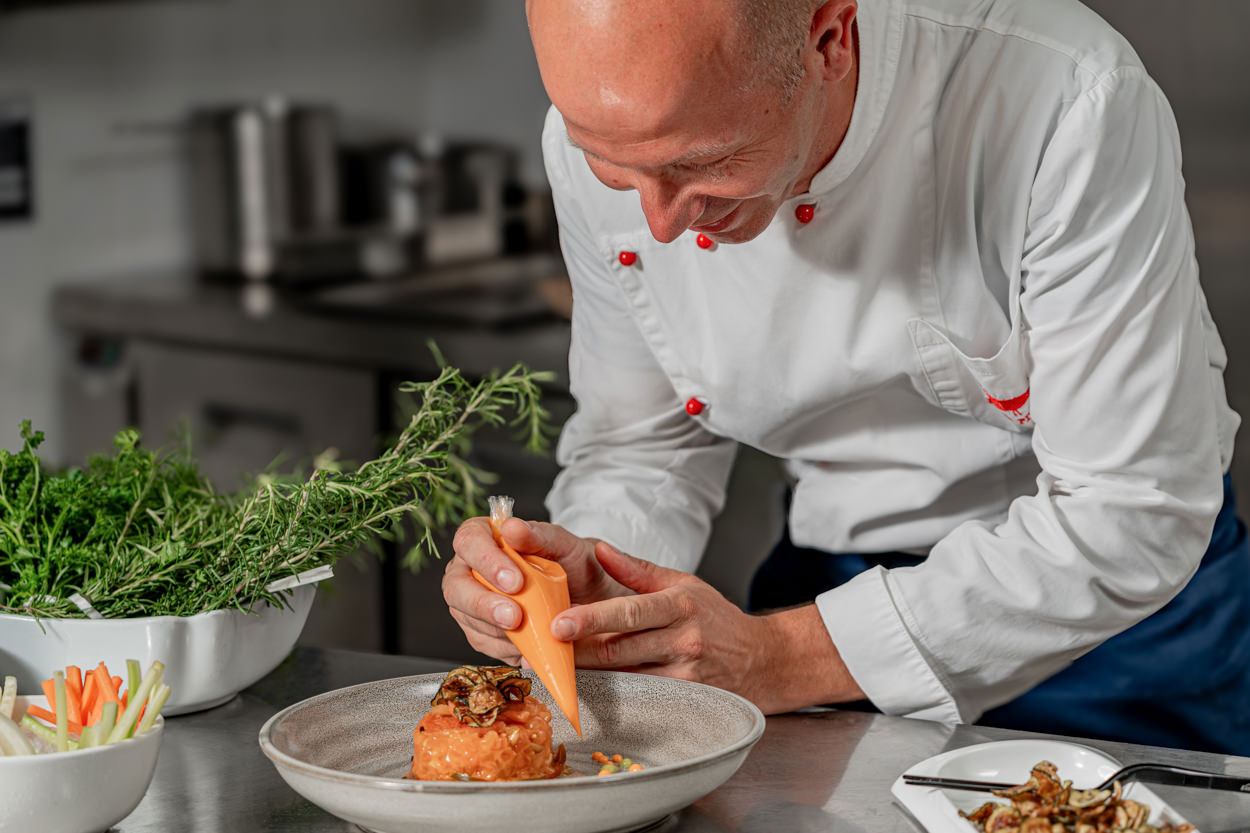 La foto, realizzata dal fotografo dell'hotel a Villasimius, ritrae lo chef mentre impiatta con precisione una tartare di pomodoro nella cucina dell'hotel. L'immagine cattura l'attenzione per i dettagli e la cura nella presentazione dei piatti, riflettendo l'alta qualità e la creatività della proposta culinaria dell'hotel. Questo scatto non solo esalta l'abilità e la passione dello chef, ma trasmette anche l'impegno dell'hotel a offrire un'esperienza gastronomica d'eccellenza. Ideale per promuovere il ristorante dell'hotel e attrarre ospiti amanti della buona cucina, questa fotografia supporta le strategie di marketing e rafforza l'immagine del brand come sinonimo di lusso e raffinatezza.