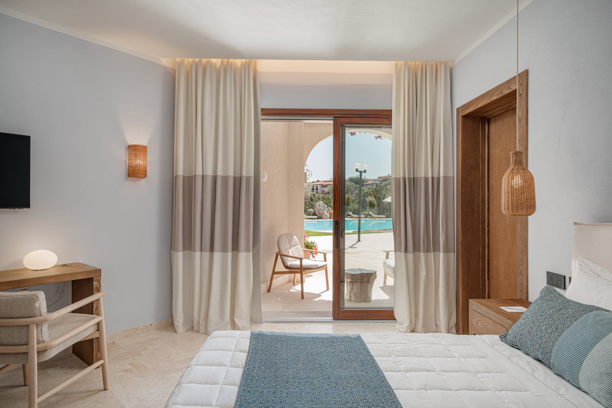 Questa foto, parte del servizio fotografico per un hotel a Orosei, immortala una camera deluxe con balcone, che offre una vista spettacolare sulla piscina dell'hotel. La camera è arredata con un raffinato mix di design moderno e dettagli che richiamano le texture della tradizione sarda, reinterpretate in chiave contemporanea. Il fotografo ha sapientemente catturato l'eleganza e il comfort della stanza, sottolineando l'attenzione dell'hotel ai dettagli e alla valorizzazione della cultura locale. Questo tipo di fotografia è essenziale per attrarre clienti in cerca di un'esperienza di soggiorno unica e autentica, contribuendo a rafforzare l'immagine del brand e a sostenere le campagne di marketing dell'hotel.
